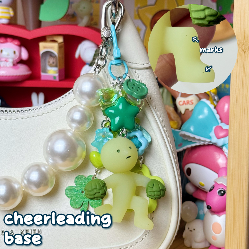 light green, dark green, & teal cheerleading base smiski keychain with small marks on left leg